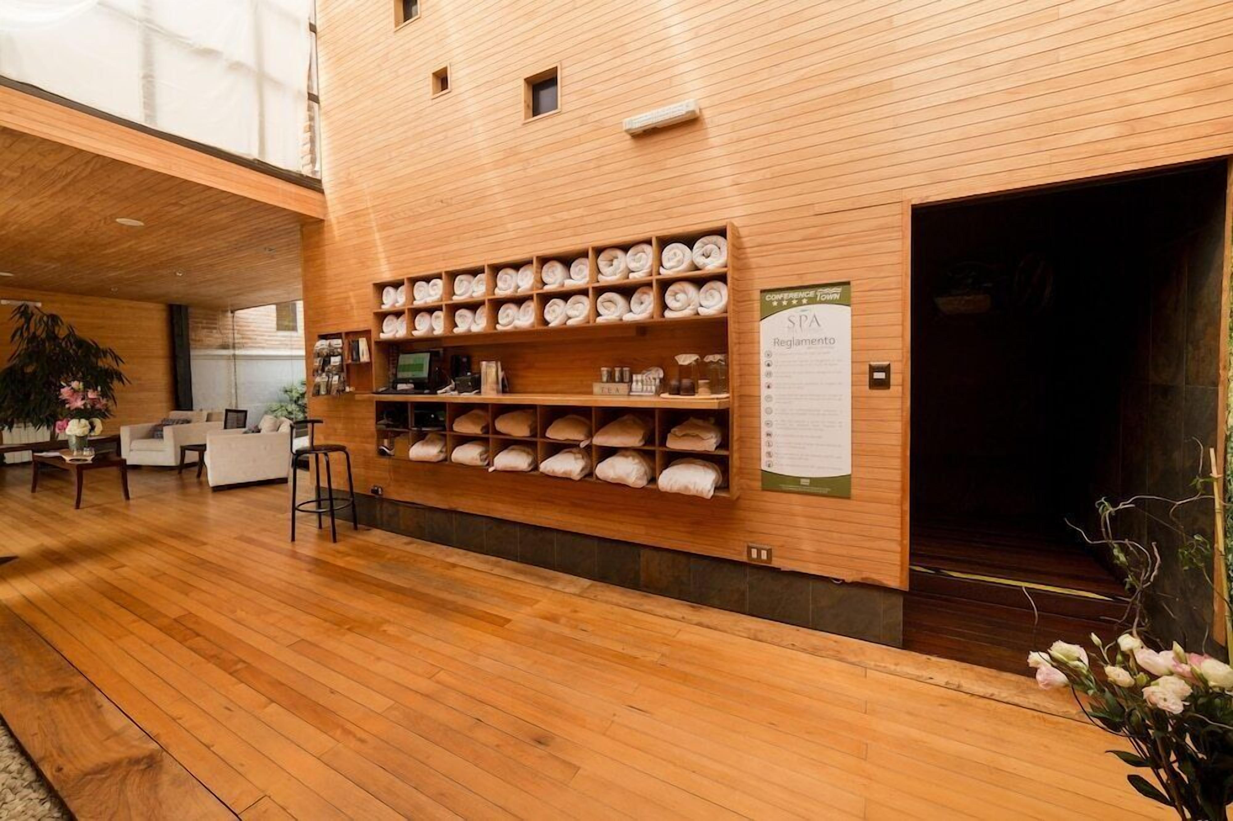 Un área de spa con paredes de madera, estantes con toallas, un mostrador de recepción y un cartel con las normas del spa.