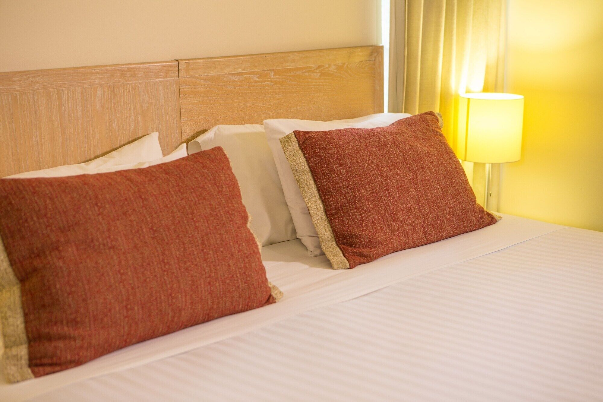 Una cama bien hecha con ropa de cama blanca y dos almohadas rojas.