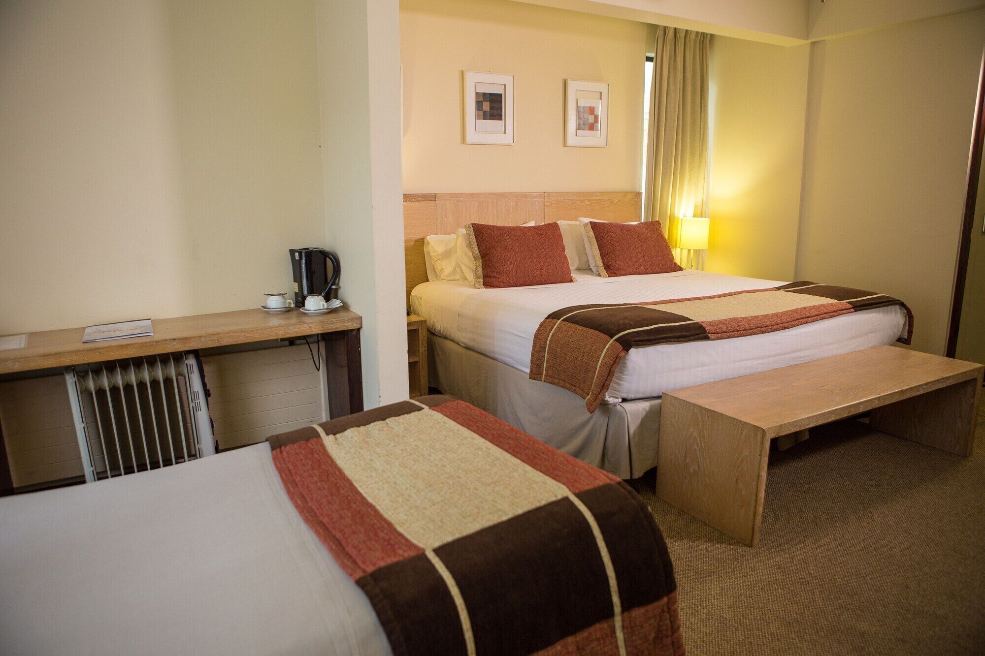 Quarto de hotel com cama, mesa de cabeceira e escrivaninha com cafeteira.