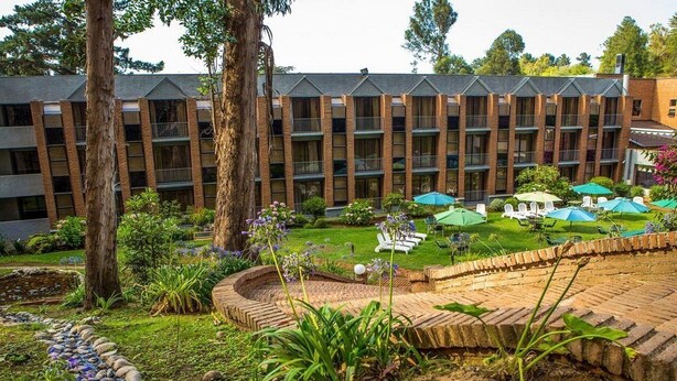 Un hotel con patio que cuenta con mesas al aire libre, un sendero de ladrillo y abundante vegetación.