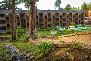 Un hotel con patio que cuenta con mesas al aire libre, un sendero de ladrillo y abundante vegetación.