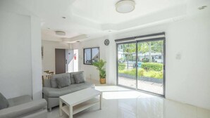 Sala de estar moderna com sofá cinzento, mesa de centro branca e uma grande porta de vidro deslizante que dá para uma varanda com vegetação.