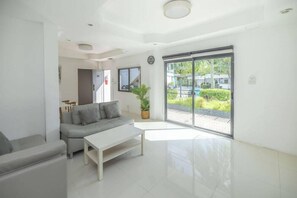 A modern living room with a grey sofa, white coffee table, and a large sliding glass door leading to a balcony with greenery. - The Coconut Nanai Resort (Patong)