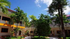 Un patio con un edificio que tiene un balcón, rodeado de palmeras y plantas en macetas.