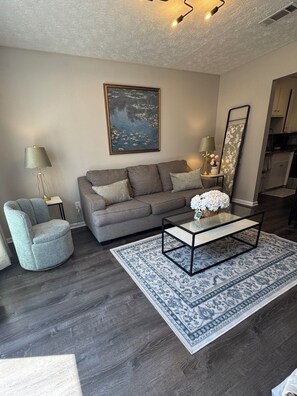 A modern living room with a sofa, armchair, coffee table, and a painting on the wall.