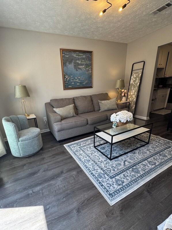 A modern living room with a sofa, armchair, coffee table, and a painting on the wall.