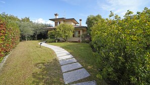 A house with a stone pathway leading to the front door, surrounded by lush greenery and trees. - Villa Riai (Moniga del Garda)