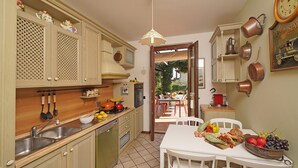 A kitchen with a dining area, featuring a sink, stove, and various kitchen utensils. - Villa Riai (Moniga del Garda)