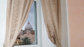 A window with beige curtains, offering a view of a building with a dome and classical architecture. - Chez Alice Vatican (Rome)