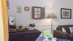 A living room with a dining table set for a meal, a sofa, a lamp, and framed pictures on the wall. - Chez Alice Vatican (Rome)