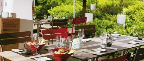 Un área de comedor al aire libre con varias mesas y sillas, algunas con sillas rojas y otras con sillas marrones.