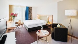 Habitación de hotel con cama, escritorio, silla, mesita, lámpara y televisor.