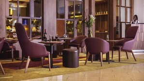 Un vestíbulo con amplios ventanales, paneles de madera y sillones tapizados en morado.