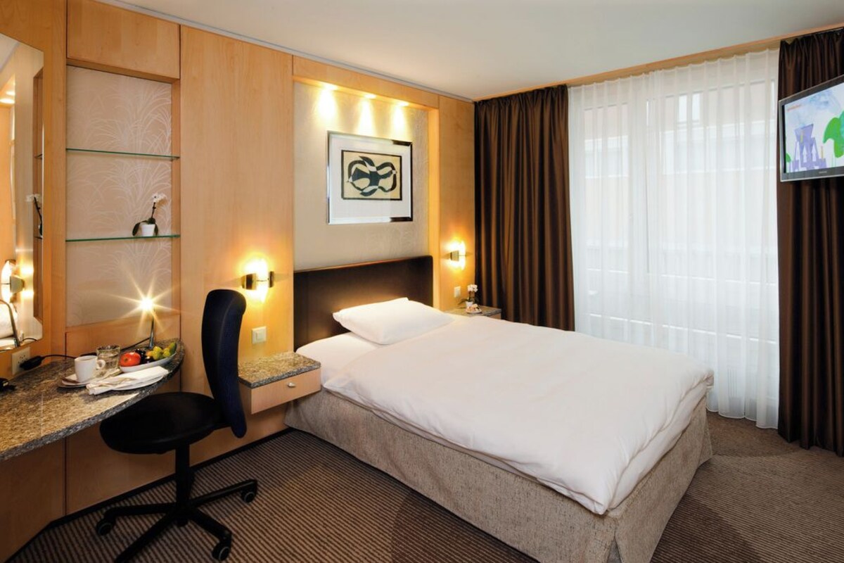 Habitació d'hotel amb llit, escriptori, cadira i televisió.