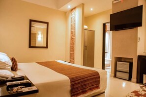 Habitación de hotel con cama, televisor de pantalla plana, minibar y puerta de baño.