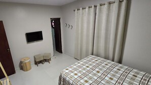 A bedroom with a bed, a wooden ladder, a small round stool, a television, and a door.