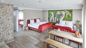A hotel room with a marble wall, a large painting of lambs, a wooden dining table with fruit, and two red beds.