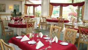 A restaurant with tables set for dining, featuring red tablecloths and wooden chairs.