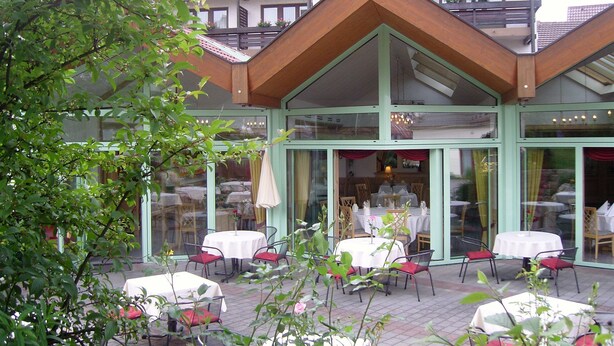 A building with a green facade, multiple balconies, and outdoor seating with tables and chairs.
