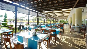 An outdoor dining area with multiple tables and chairs, covered by a wooden roof structure. - Perre Delta Hotel (Alanya)