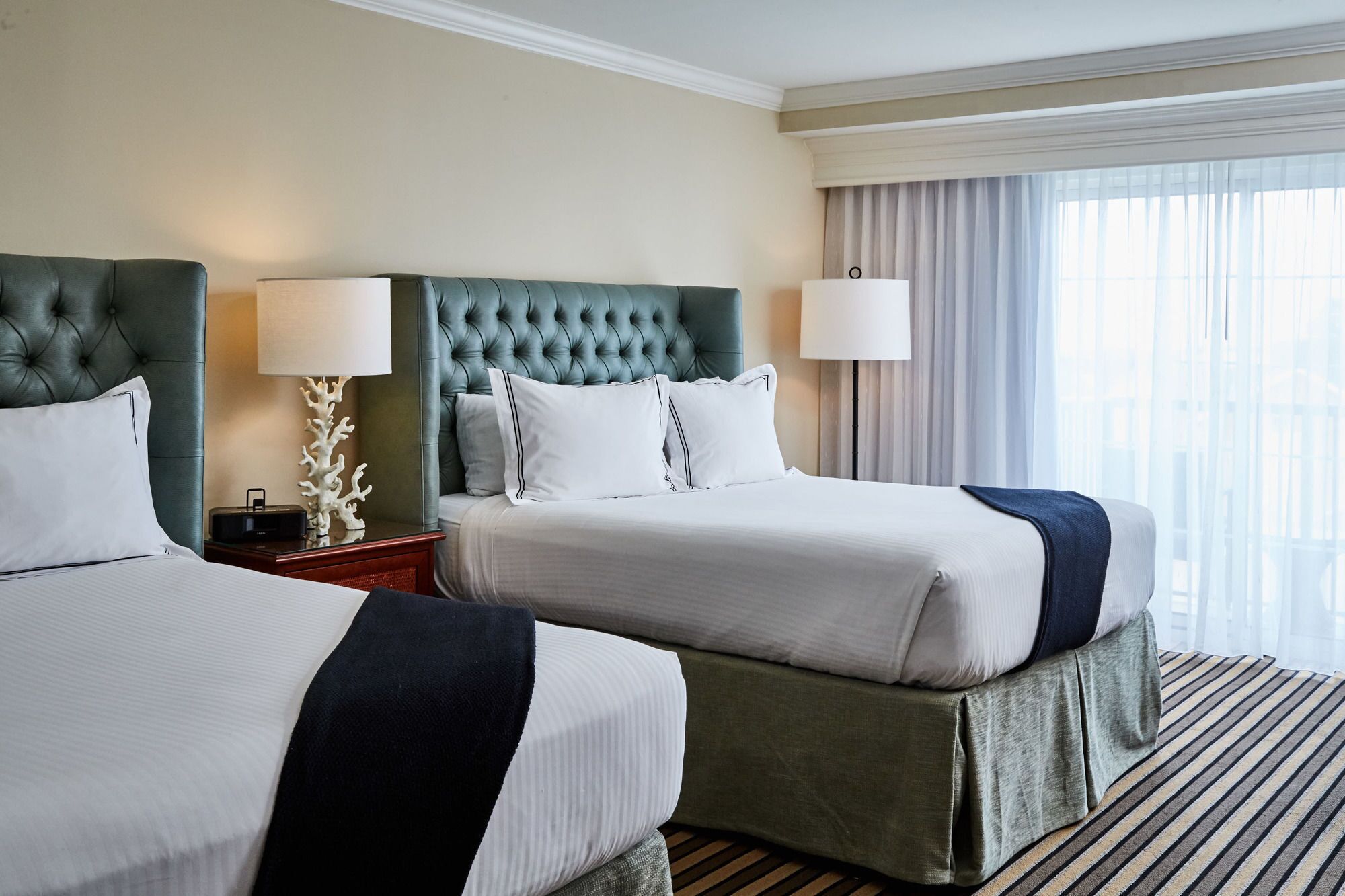 A hotel room with two beds, each with a tufted headboard, white linens, and a striped rug.