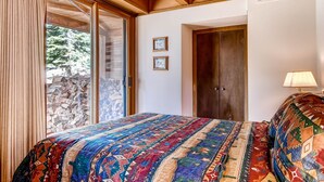 Un dormitorio con una cama grande, vigas de madera en el techo, una ventana con cortinas y una puerta.