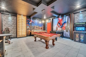 Uma mesa de bilhar em um ambiente com parede de tijolos e um mural do Homem-Aranha.