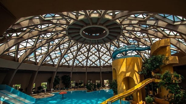Una piscina interior con un gran tobogán central y un techo circular de cristal.