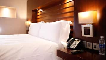 Une chambre d’hôtel équipée d’un lit, de lampes de chevet, d’un téléphone, d’une bouteille d’eau et d’un luminaire fixé au mur.