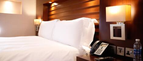 A hotel room with a bed, bedside lamps, a phone, a water bottle, and a wall-mounted light fixture.