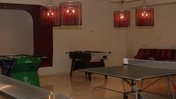 A room with a foosball table, ping pong table, and a green Heineken pool table.