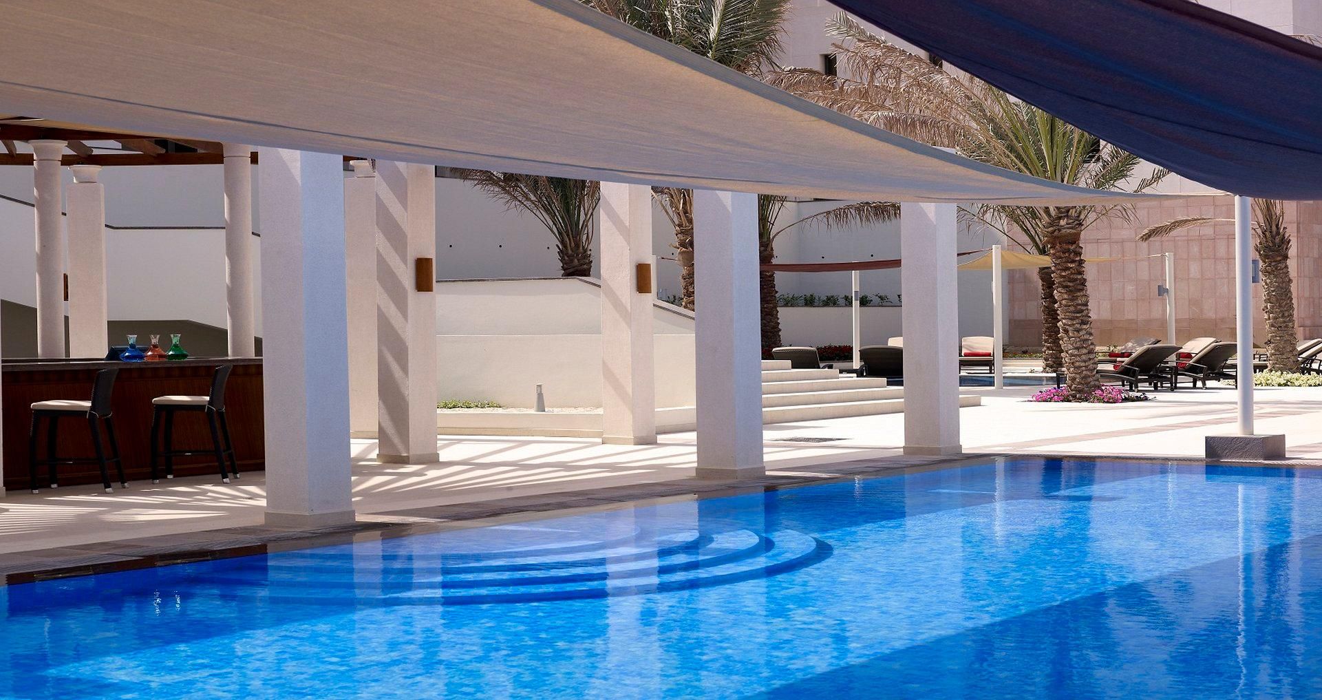 A swimming pool with a sunshade, lounge chairs, and a bar area.