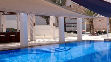 A swimming pool with a sunshade, lounge chairs, and a bar area.