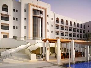 A hotel with a pool, outdoor seating, and a staircase leading to the upper floors. - Crowne Plaza Sohar (Sohar)