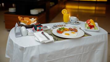 Una mesa de desayuno con un cesto de pan, un plato de huevos, un vaso de zumo de naranja y un bol de ensalada.