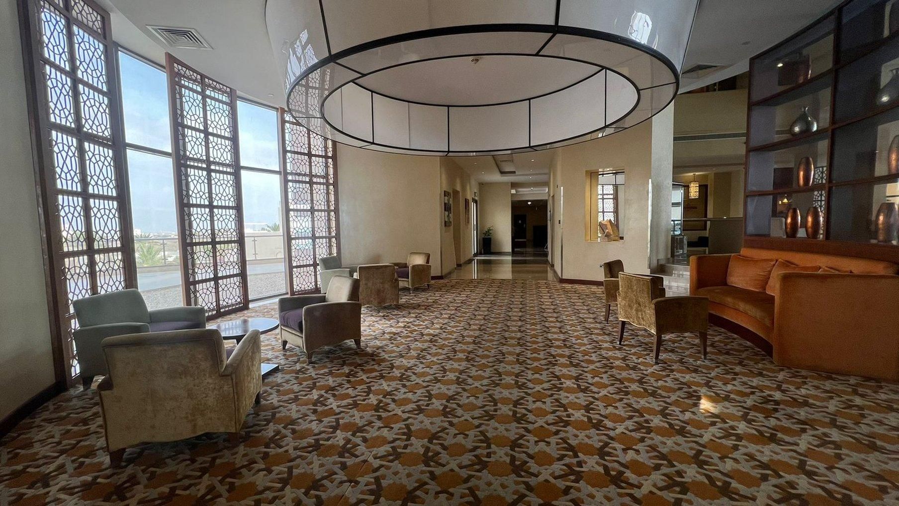 Eine geräumige Lobby mit Musterfliesen, Sitzbereichen und großen Fenstern mit dekorativen Sichtschutzvorrichtungen.
