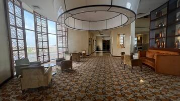 Eine geräumige Lobby mit Musterfliesen, Sitzbereichen und großen Fenstern mit dekorativen Sichtschutzvorrichtungen.
