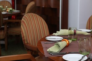 A dining table set with plates, cutlery, and glasses, surrounded by striped chairs. - Crowne Plaza Sohar (Sohar)