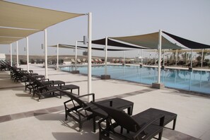 A poolside area with lounge chairs and tables, shaded by large canopies, and a clear view of the pool. - Crowne Plaza Sohar (Sohar)