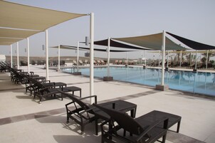 A poolside area with lounge chairs and tables, shaded by large canopies, and a clear view of the pool.