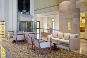 A spacious lobby with a high ceiling, a seating area with chairs and a sofa, a patterned floor, and a large pillar.