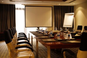 A conference room with a long table, chairs, a projector screen, and water bottles. - Crowne Plaza Sohar (Sohar)