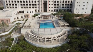A hotel with a central swimming pool, a covered seating area, and a large building in the background. - Crowne Plaza Sohar (Sohar)