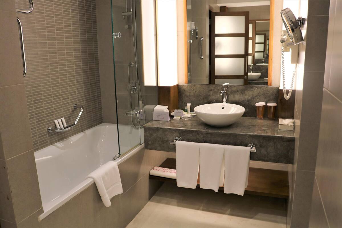 A modern bathroom with a glass-enclosed shower, a white bathtub, a marble countertop, and a large mirror.