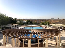 Un área de piscina con un pérgola de madera, sillas de descanso y vistas al paisaje.