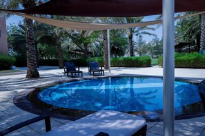 A swimming pool with lounge chairs, surrounded by palm trees and a shaded area. - Crowne Plaza Sohar (Sohar)