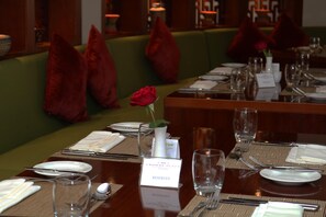 A restaurant setting with tables set for dining, a green cushioned bench, and red pillows.