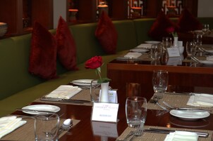 A restaurant setting with tables set for dining, a green cushioned bench, and red pillows.