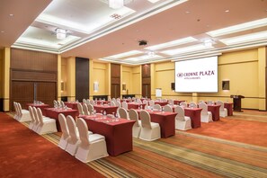A conference room with rows of tables and chairs, a podium, and a screen displaying 'CROWNE PLAZA HOTELS & RESORTS' branding. - Crowne Plaza Sohar (Sohar)