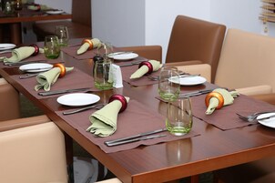 Una mesa de comedor dispuesta con platos, cubiertos y vasos, con servilletas dobladas sobre posavasos.